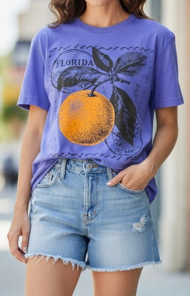 A woman wearing a purple graphic t-shirt with a large orange and leaf design and the word 'FLORIDA' on the front, paired with light-wash denim shorts.