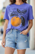 A woman wearing a purple graphic t-shirt with a large orange and leaf design and the word 'FLORIDA' on the front, paired with light-wash denim shorts.