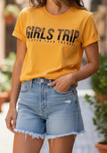 Person wearing a yellow 'Girls Trip' t-shirt and denim shorts outdoors.