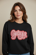 A woman wearing a black crewneck sweatshirt with a red and white gingham check graphic spelling 'gooya' in cursive script across the chest, set against a plain beige background.