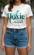 Person wearing a white t-shirt with 'Doxie Club Stay Long' text and blue shorts.