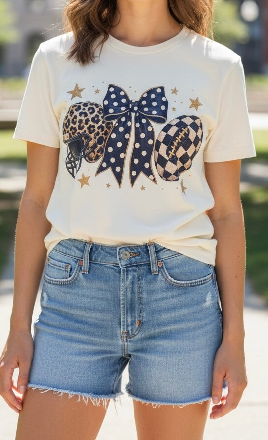 A woman wearing a cream graphic t-shirt with a navy blue polka dot bow, leopard print football helmet, checkered football, and gold stars, paired with light-wash denim shorts.