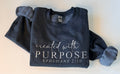 Folded dark gray sweatshirt with 'created with PURPOSE EPHESIANS 2:10' text on a light background