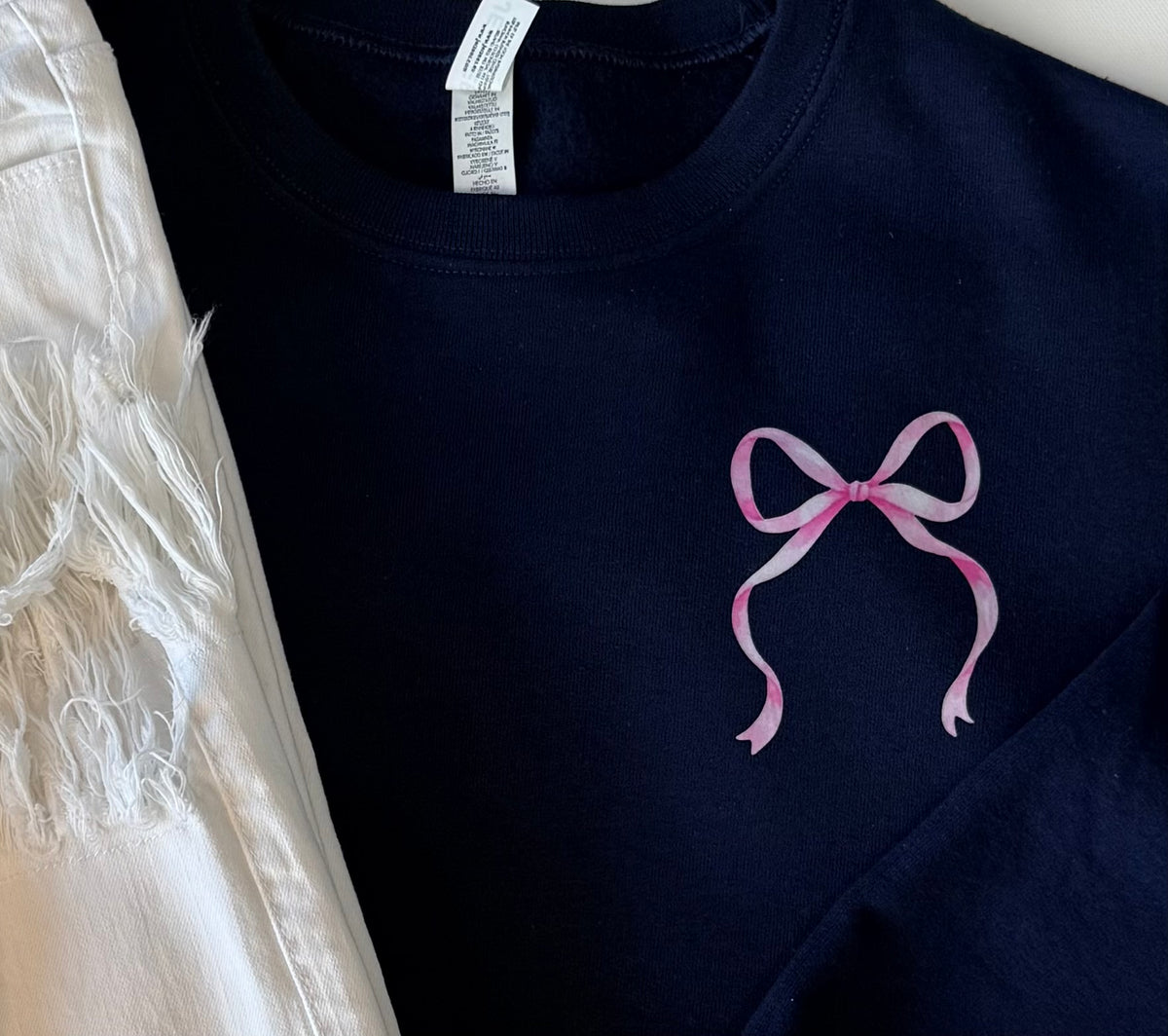 Close-up of the bow.  Navy blue sweatshirt with a pink bow design on a white background