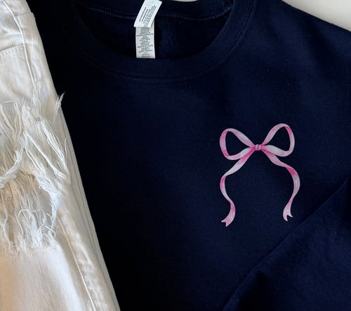 Close-up of the bow.  Navy blue sweatshirt with a pink bow design on a white background