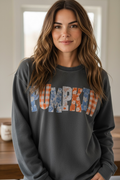 A woman wearing a dark gray crewneck sweatshirt with the word 'PUMPKIN' printed across the chest in a patchwork pattern of orange, blue, and white.