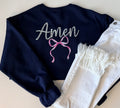 Navy blue sweatshirt with 'Amen' and a pink bow design on a light background
