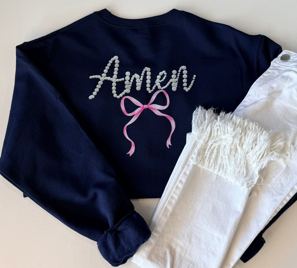 Navy blue sweatshirt with 'Amen' and a pink bow design on a light background