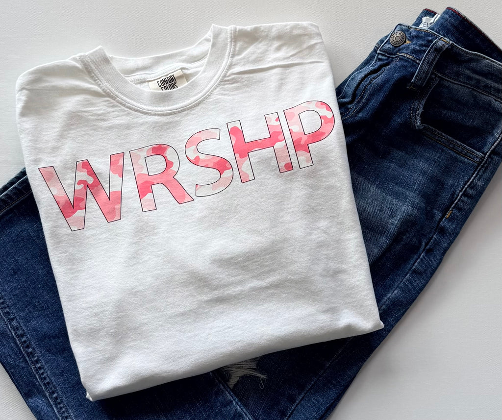 Folded white t-shirt with pink 'WRSHP' design on blue jeans