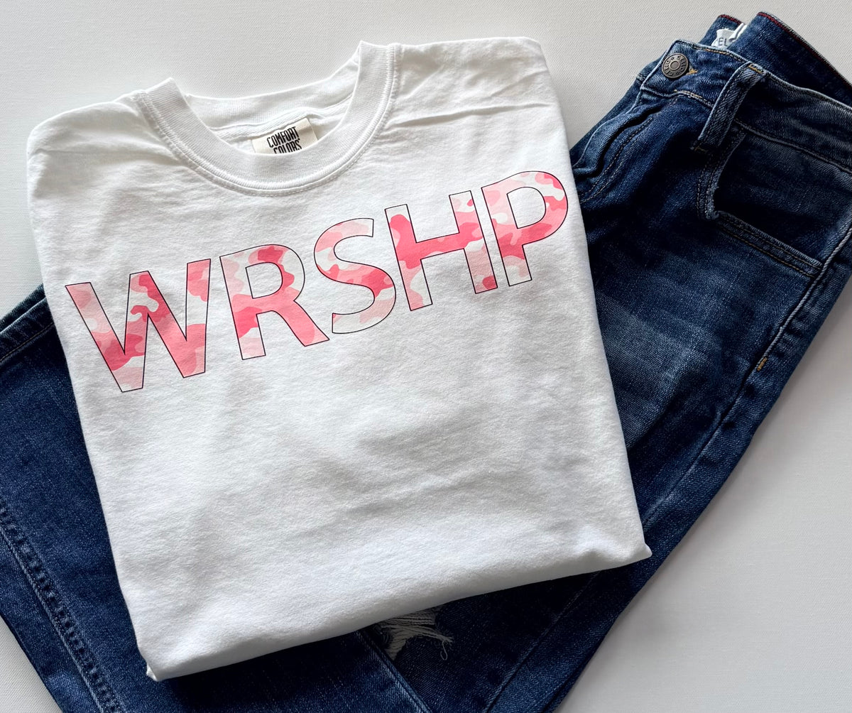Folded white t-shirt with pink 'WRSHP' design on blue jeans